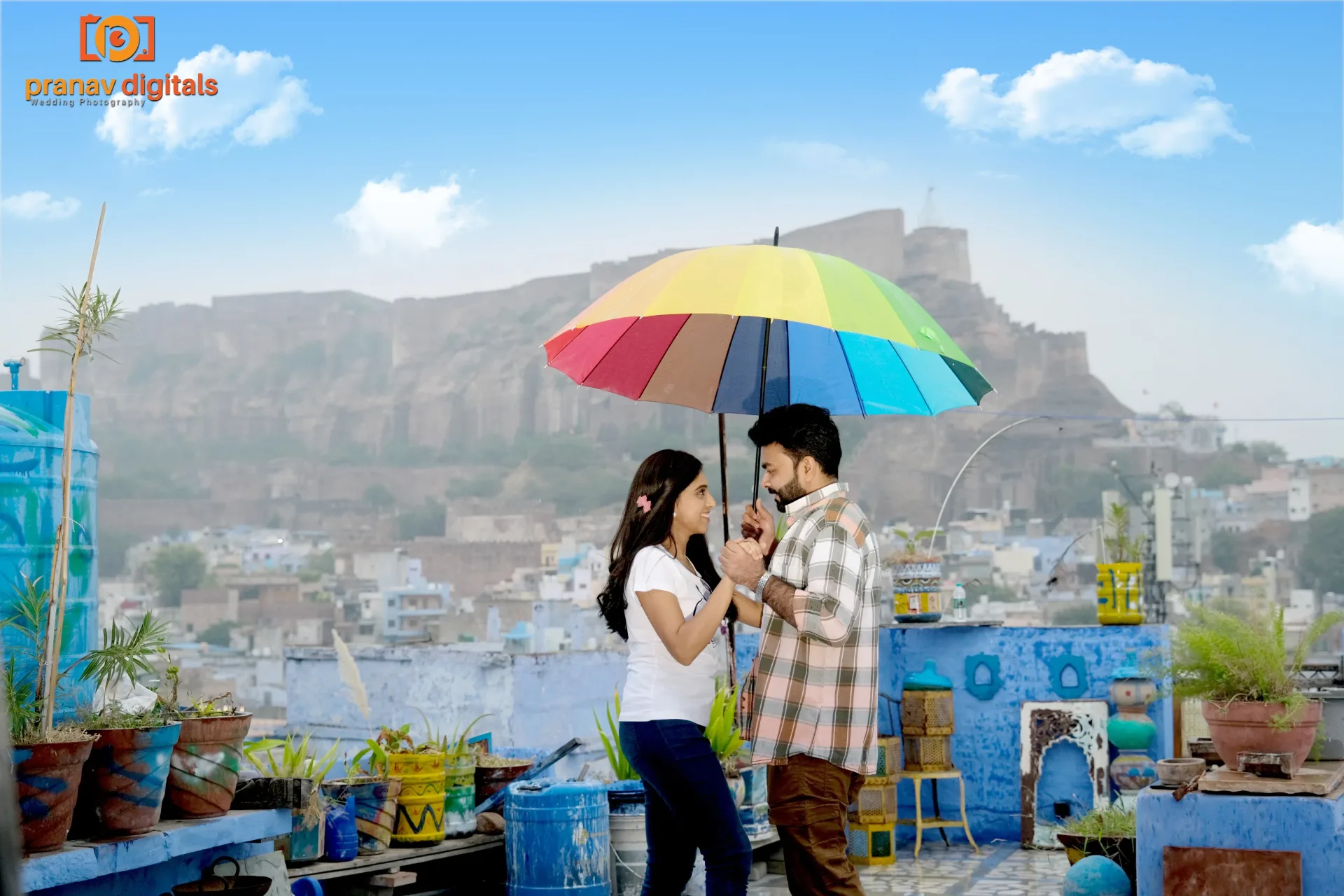 Couple under a colorful umbrella on a rooftop with city view.