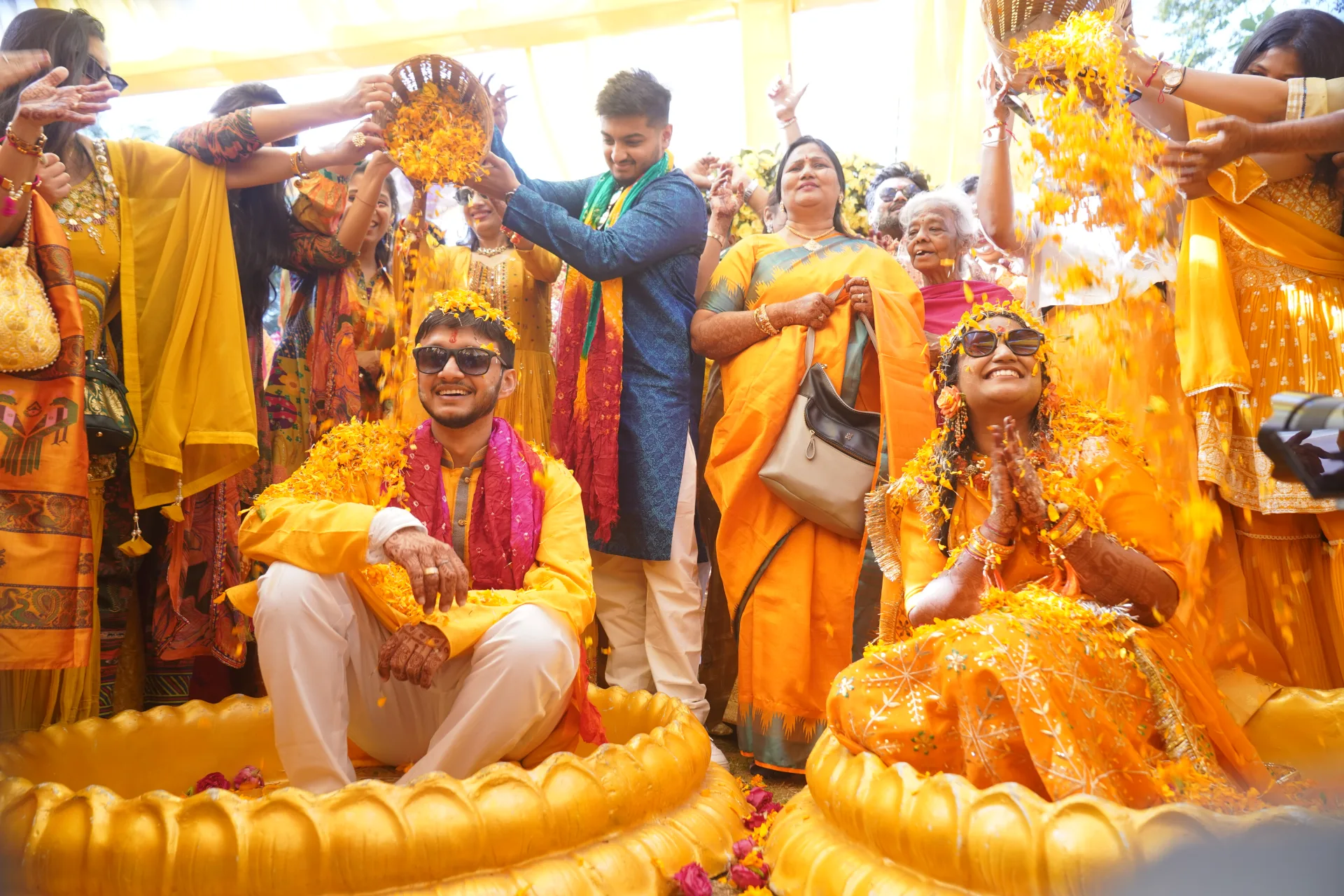 Couple celebrating with guests, adorned in yellow and flower petals.